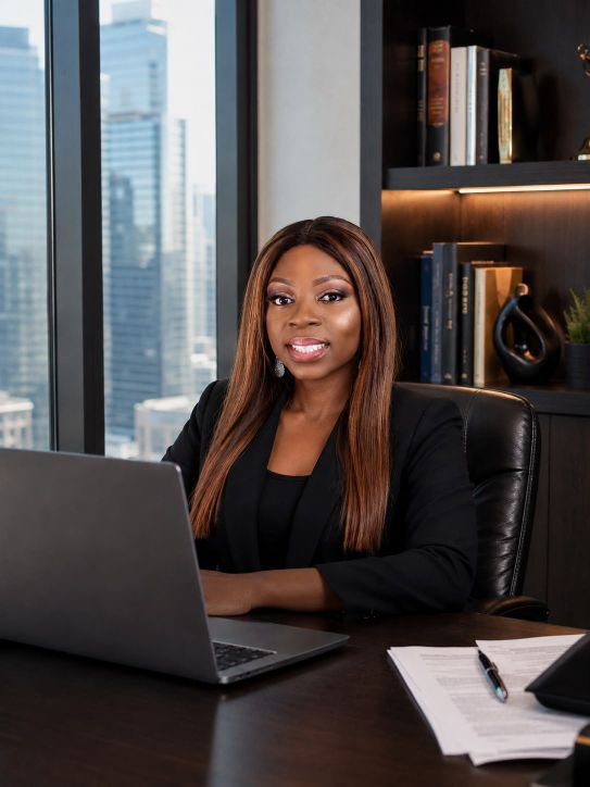 Shola Adekoya, Legal Operations Director at Civitas Law, at her desk with Toronto skyline behind her